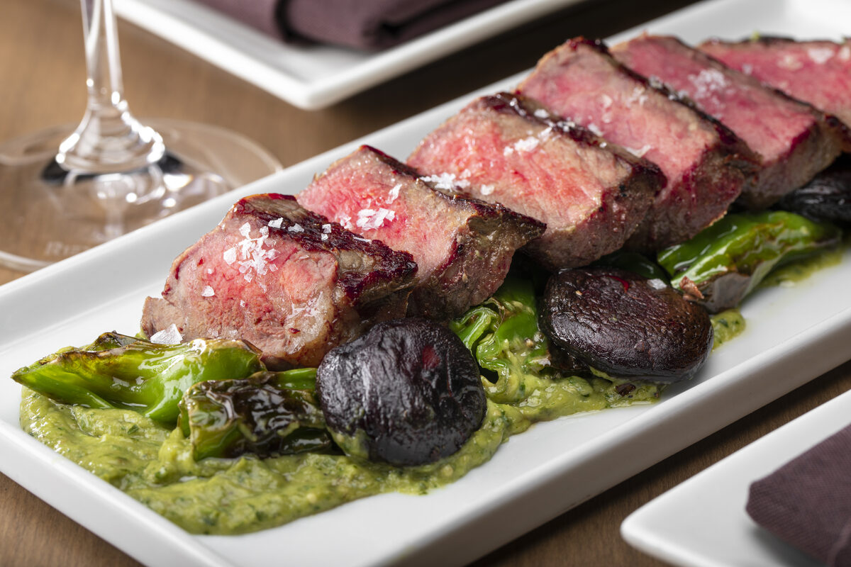 Sliced medium-rare sirloin steak with blistered shishitos and salsa verde
