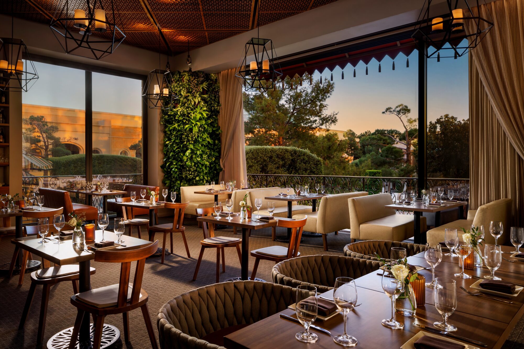 La Cave's Garden Lounge at golden hour, floor-to-ceiling windows and woven banquettes